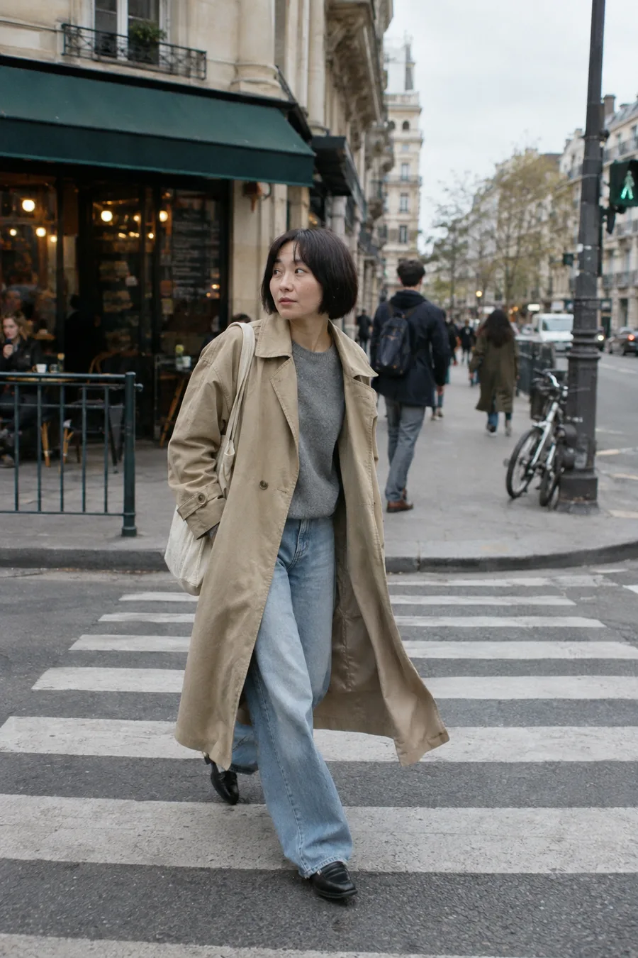 The same woman, styled by Sofi, crossing a street in a trench coat and wide jeans